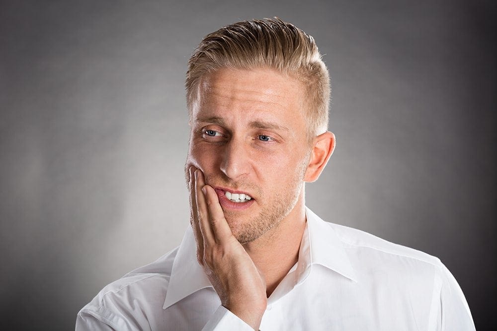 man rubbing jaw because of tooth pain